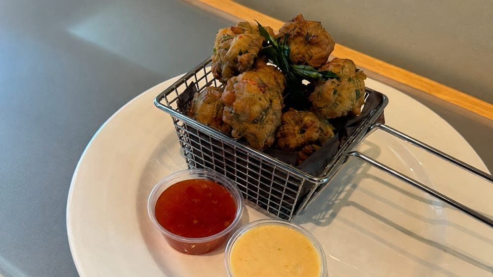 Golden fritters in a wire basket with red and yellow dipping sauces