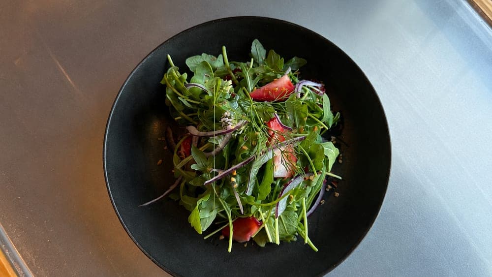 Garden greens with sliced strawberries and red onion in a black bowl