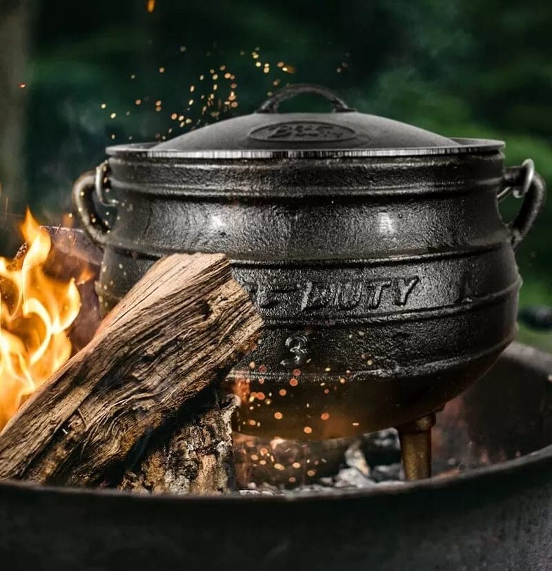 A cast-iron three-leg pot over an open fire, the traditional way to cook oildown