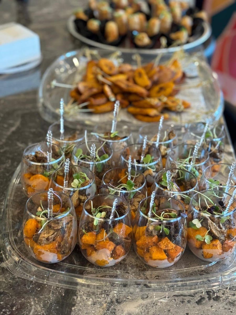 Rows of appetizer cups topped with herbs beside trays of stuffed mushrooms and pastries