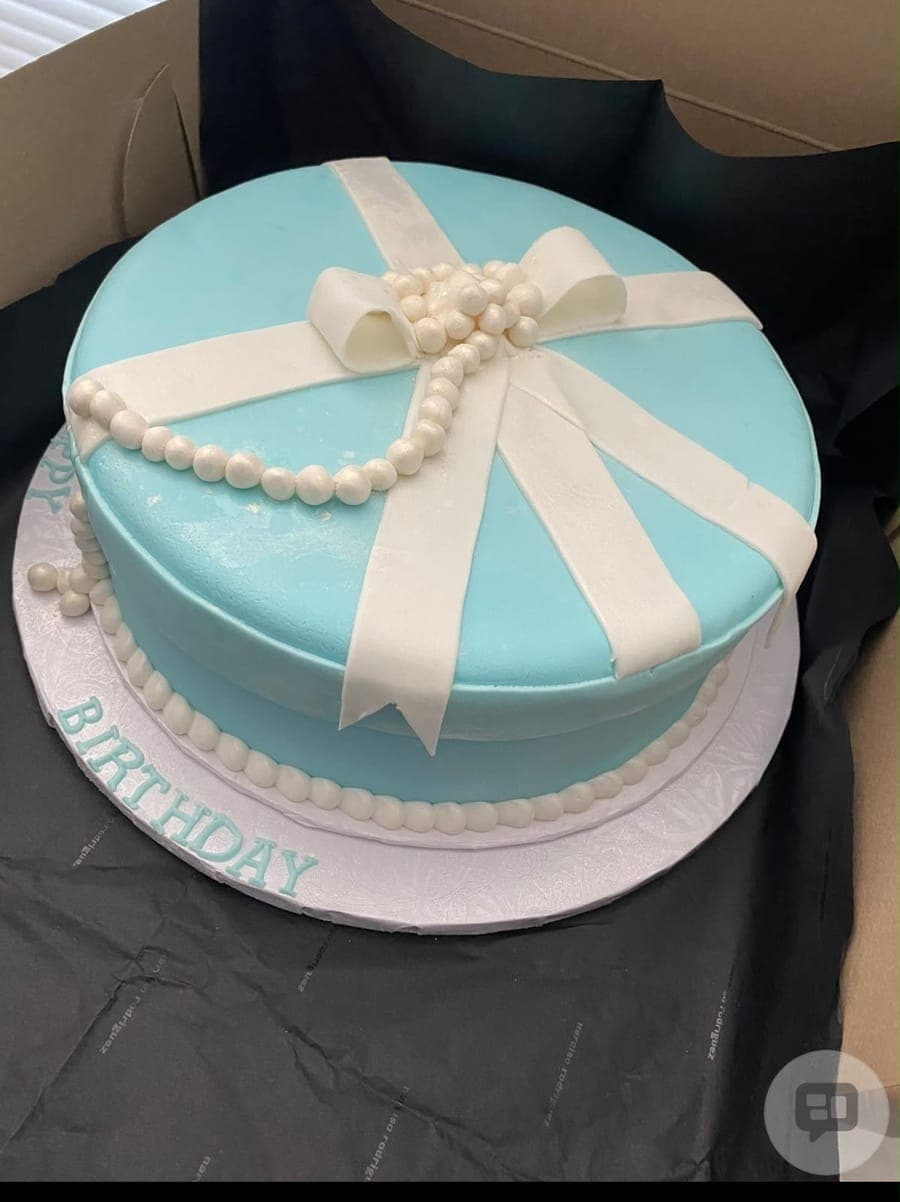 A turquoise birthday cake wrapped in a white fondant ribbon and bow with pearl trim