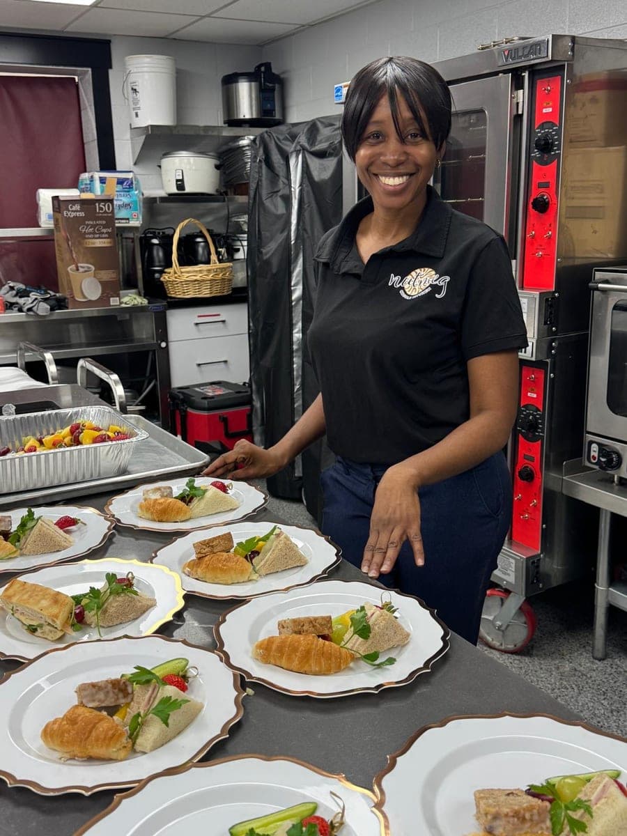 A smiling member of the Nutmeg team presenting plated sandwiches and pastries in the kitchen