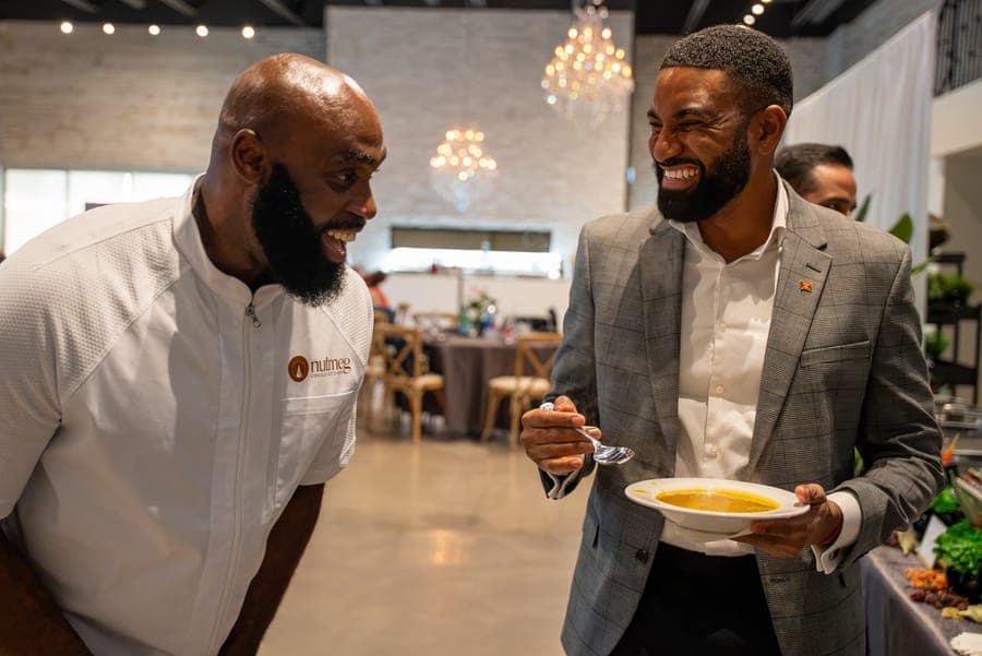 A Nutmeg chef sharing a laugh with a guest tasting a cup of soup at an event