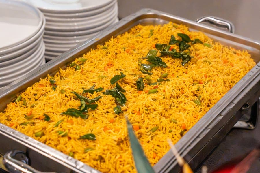 A catering tray of saffron rice with peppers and fresh herbs