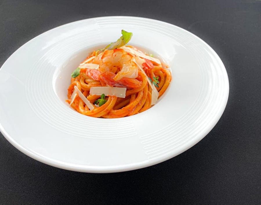 Shrimp spaghetti in tomato sauce with shaved parmesan in a white bowl