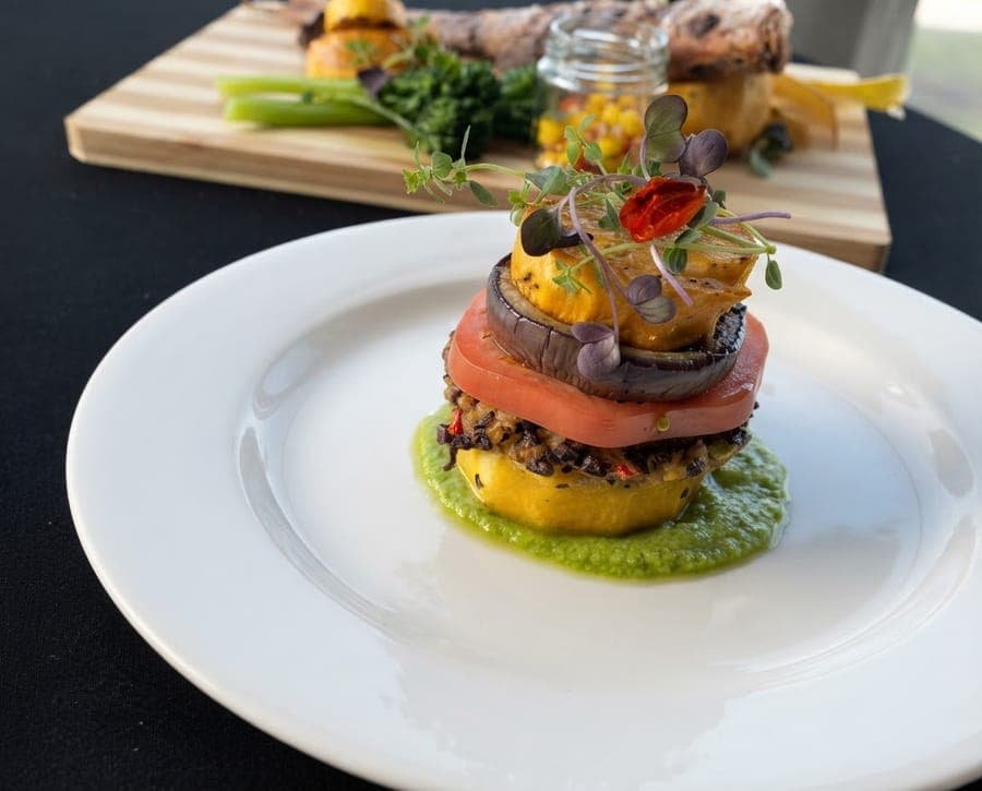 A stacked tower of grilled vegetables on herb sauce, garnished with microgreens